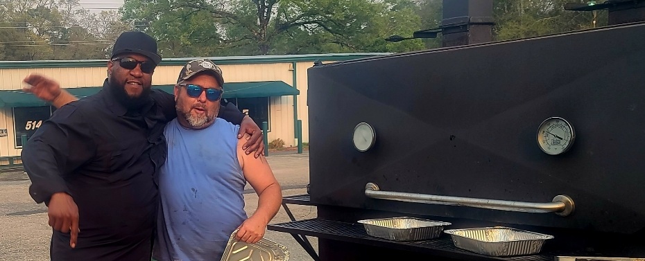 Ben Maxwell and a friend standing by a large black barbecue smoker
